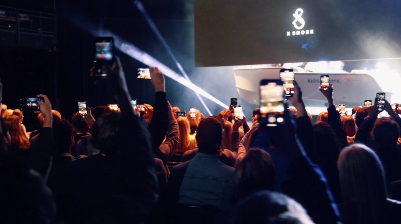 a crowd of people holding up their phones in front of a screen with the number 8 on it