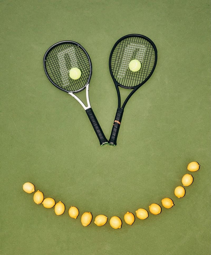 two tennis rackets and tennis balls are arranged in the shape of a smiley face .