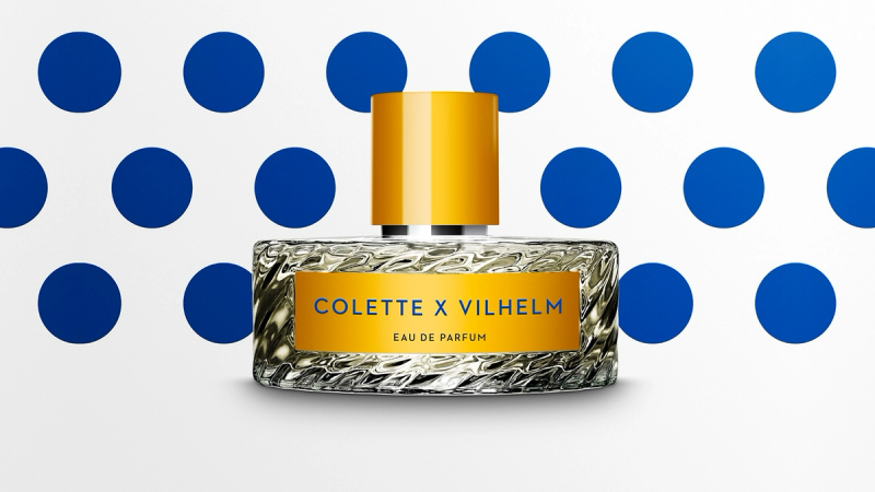 Colette X Vilhelm perfume bottle with a yellow cap and label, on a white background with blue polka dots.