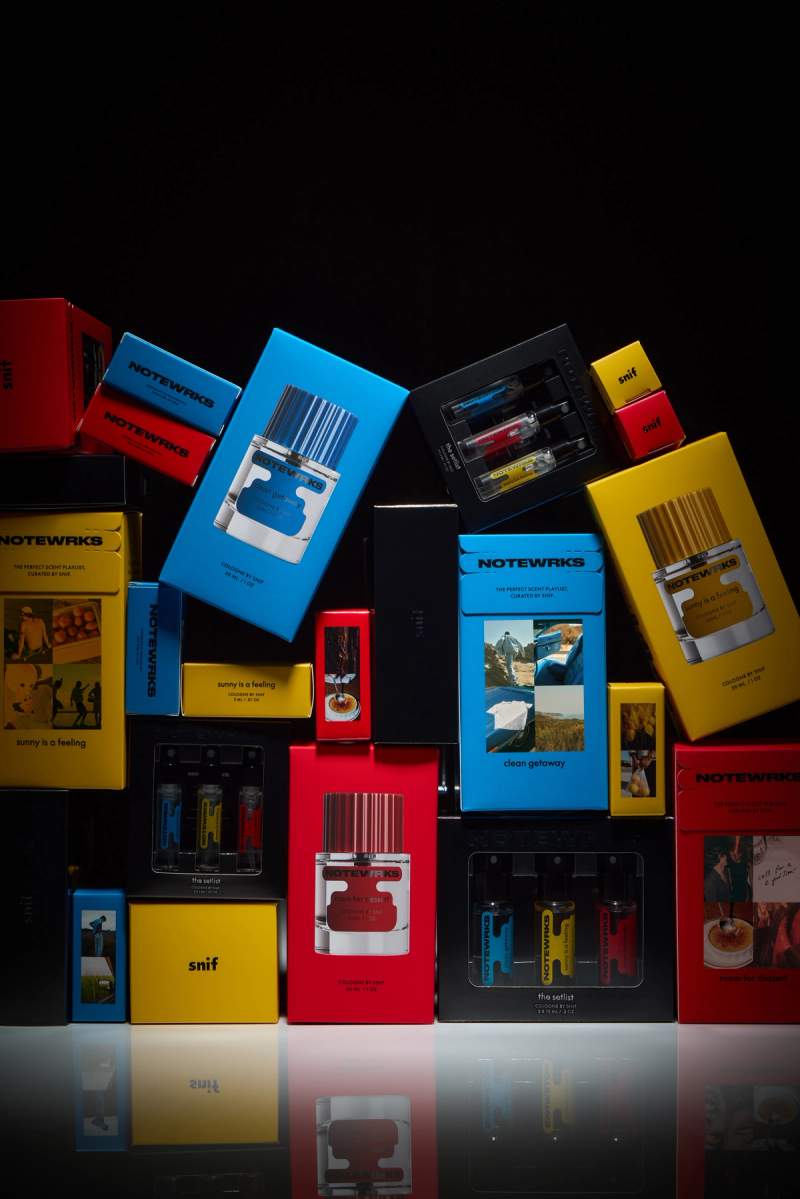 A colorful collection of perfume bottles and boxes from brands "NOTEWRKS" and "snif" on a reflective surface.