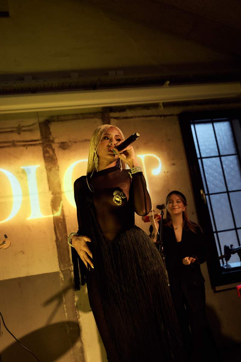 a woman singing into a microphone in front of a sign that says dior