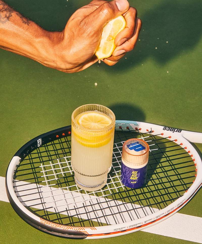 a person is squeezing a lemon into a glass next to a tennis racket .