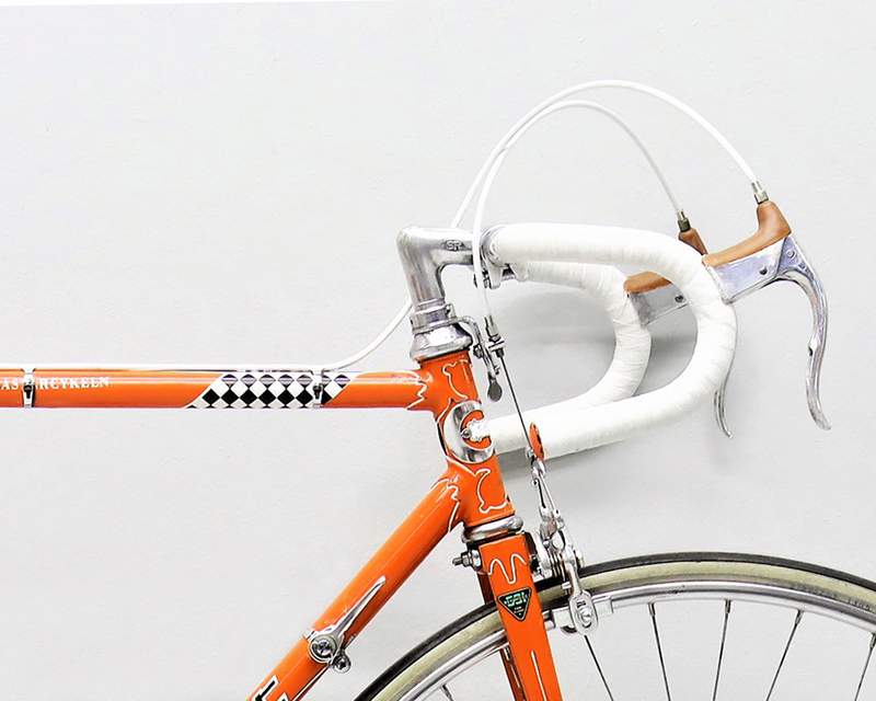 a close up of an orange bicycle with white handlebars against a white wall .