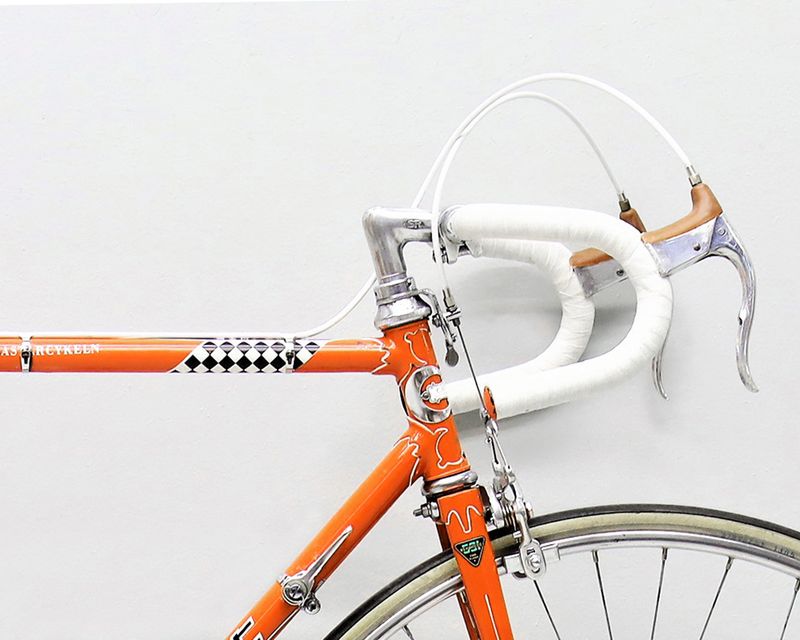 a close up of an orange bicycle with white handlebars against a white wall .
