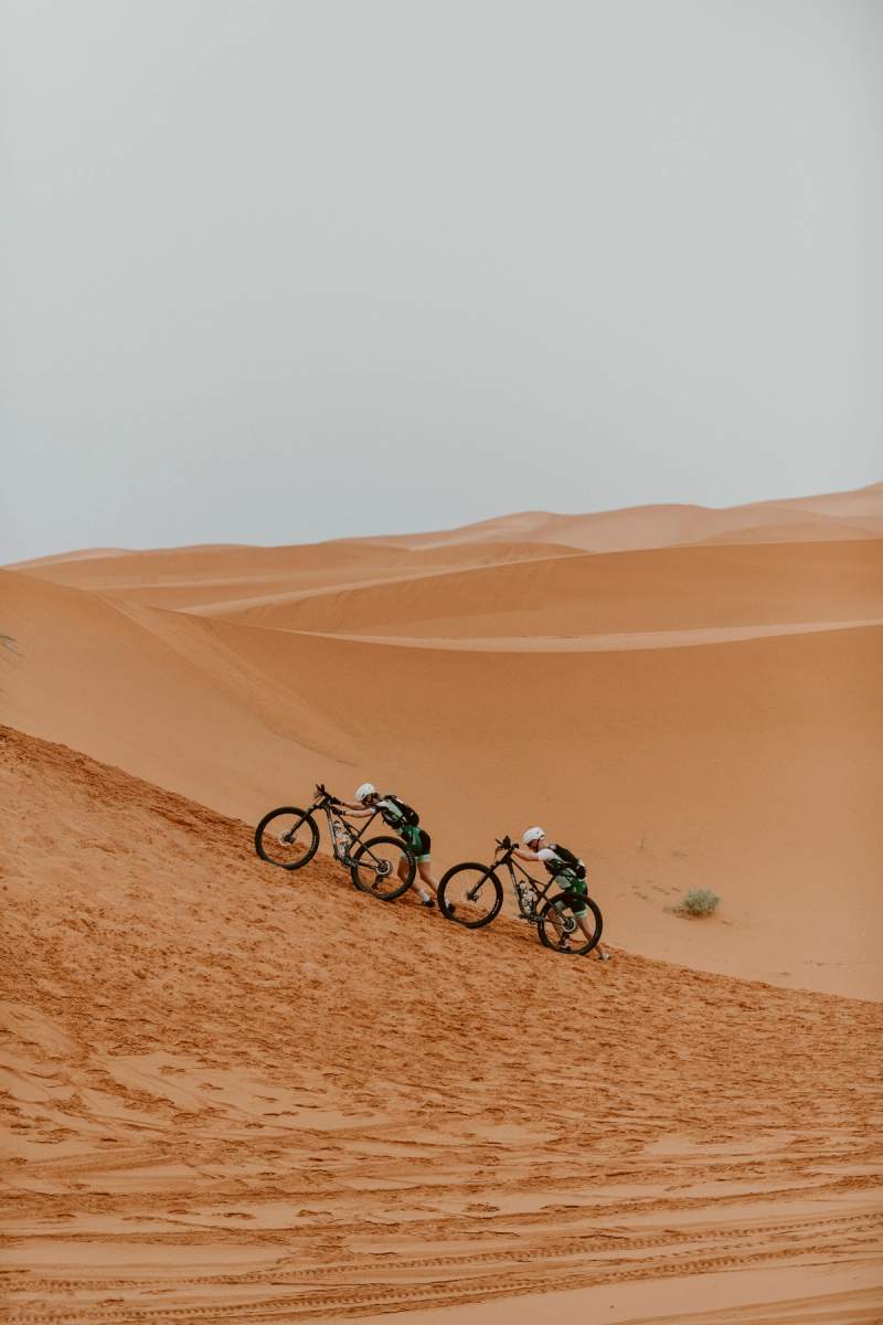 two people are riding bicycles down a sand dune in the desert .