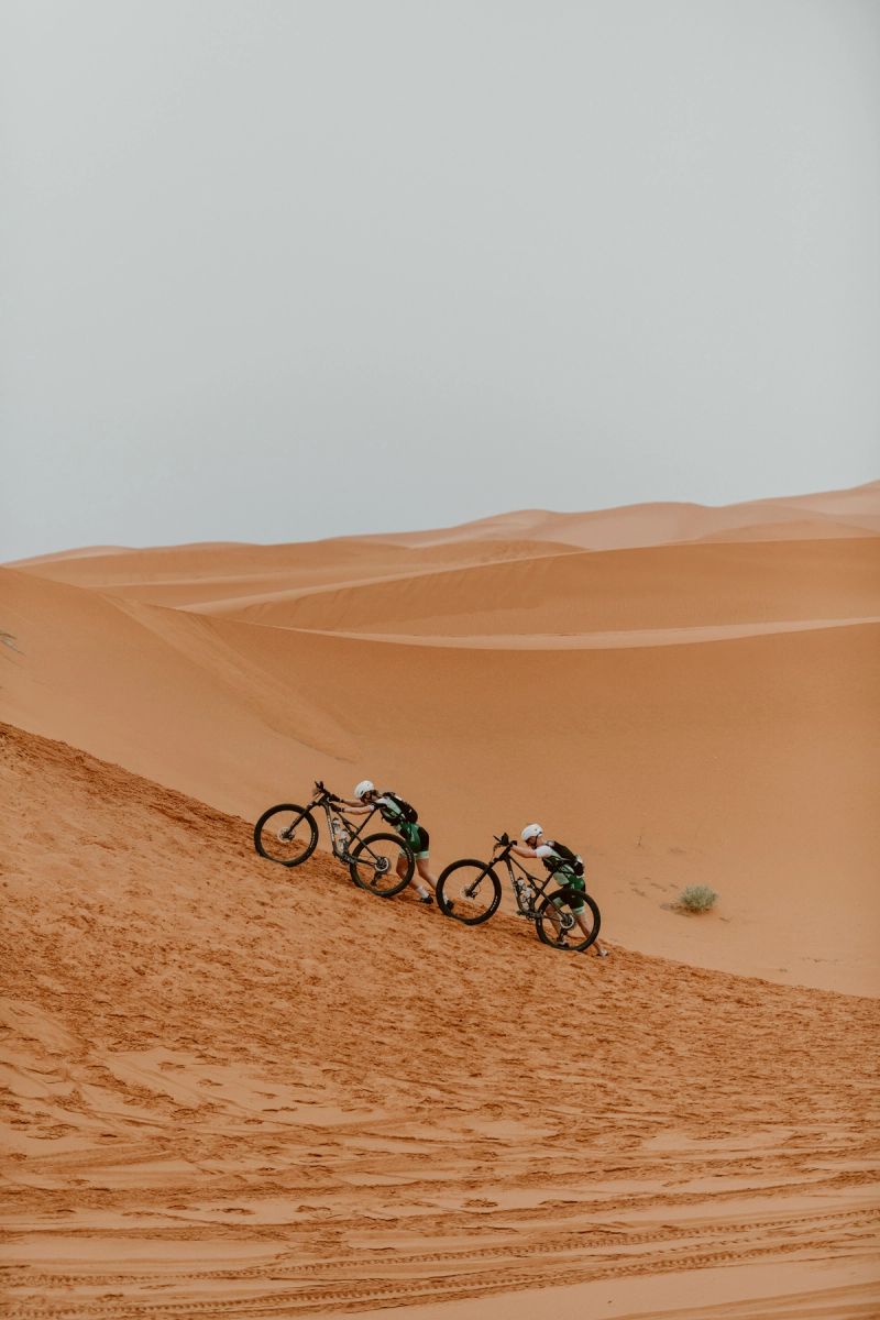 two people are riding bicycles down a sand dune in the desert .