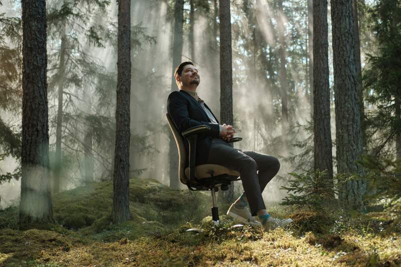 a man is sitting in an office chair in the middle of a forest .