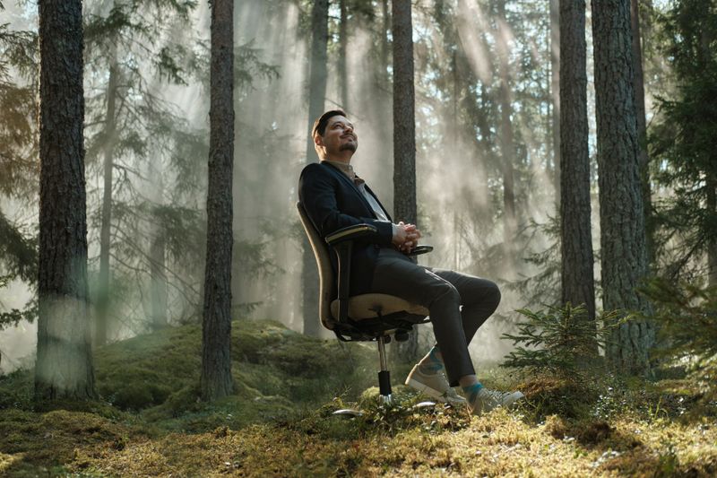 a man is sitting in an office chair in the middle of a forest .