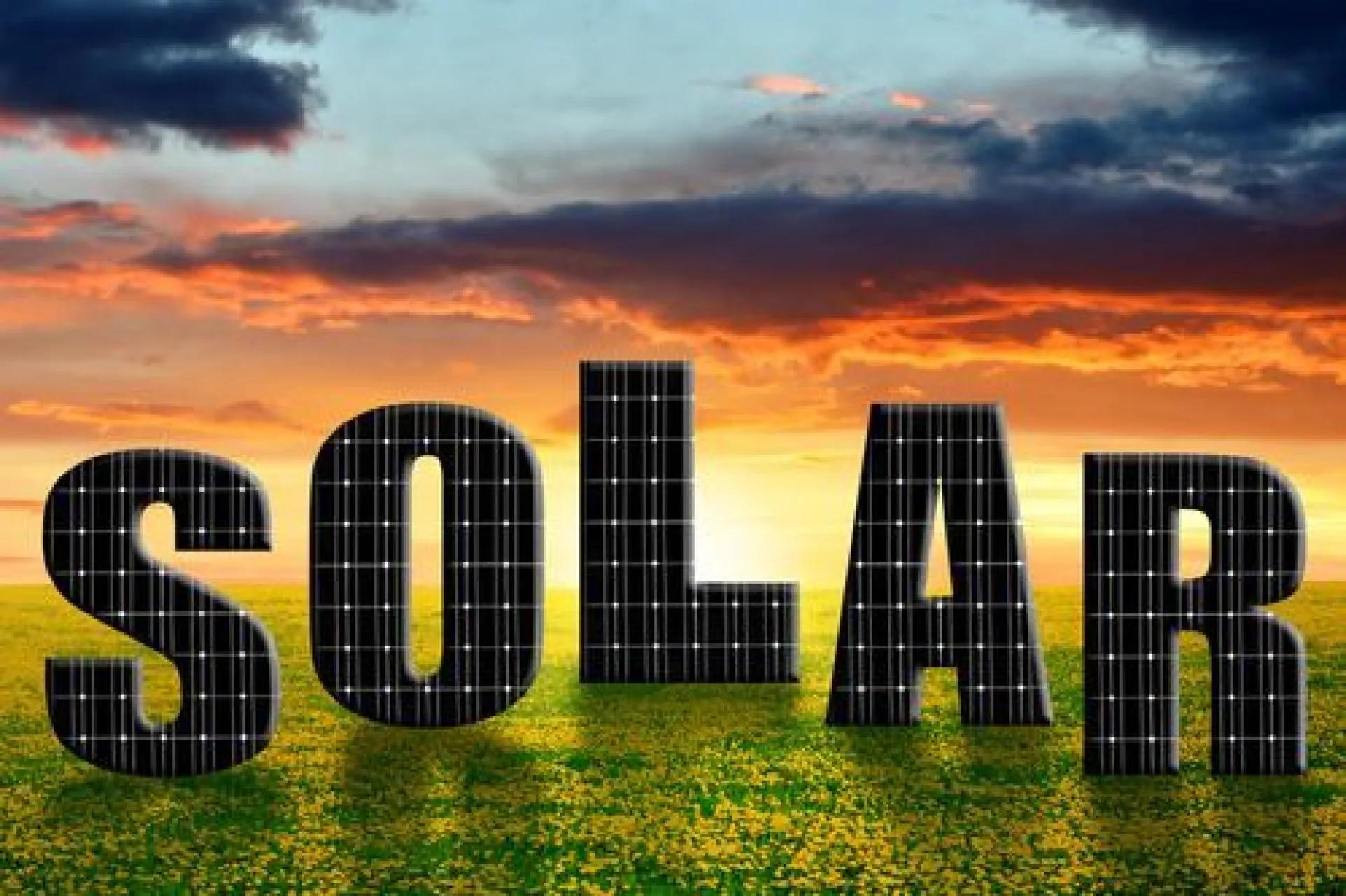The word SOLAR built from solar panels in a field at sunset