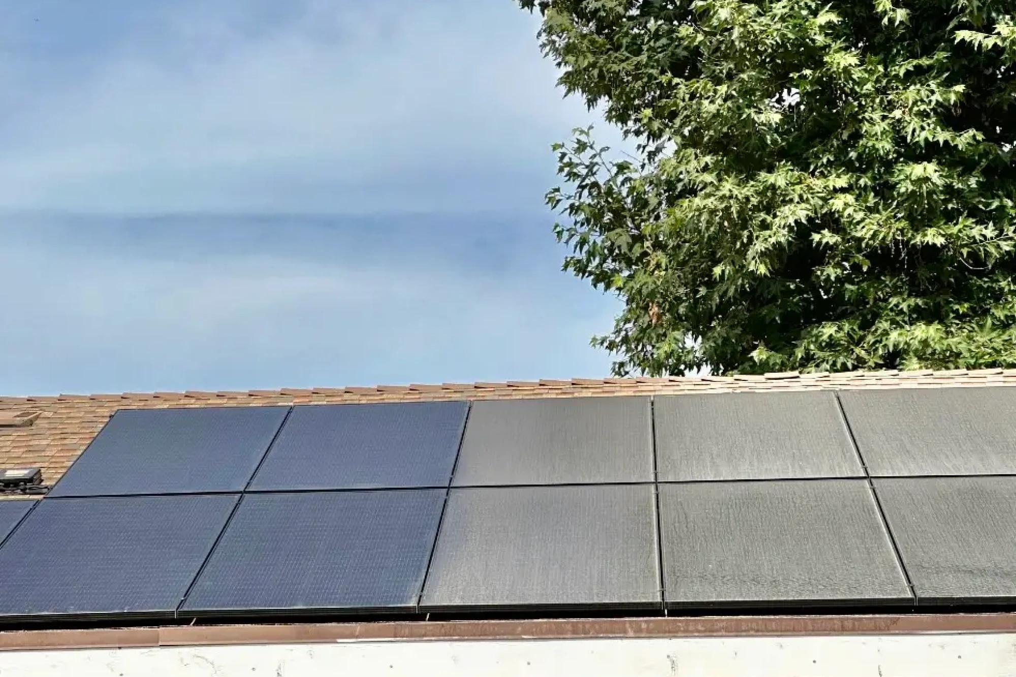 Row of black solar panels along a roof edge under a blue sky