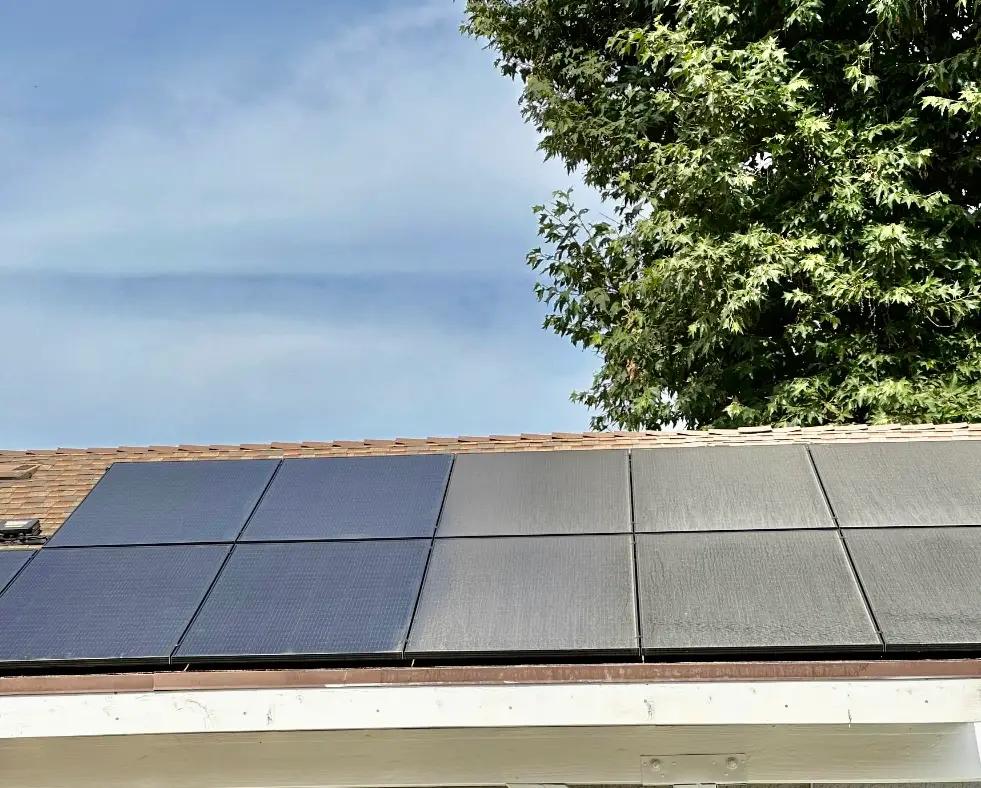 Row of black solar panels along a roof edge under a blue sky