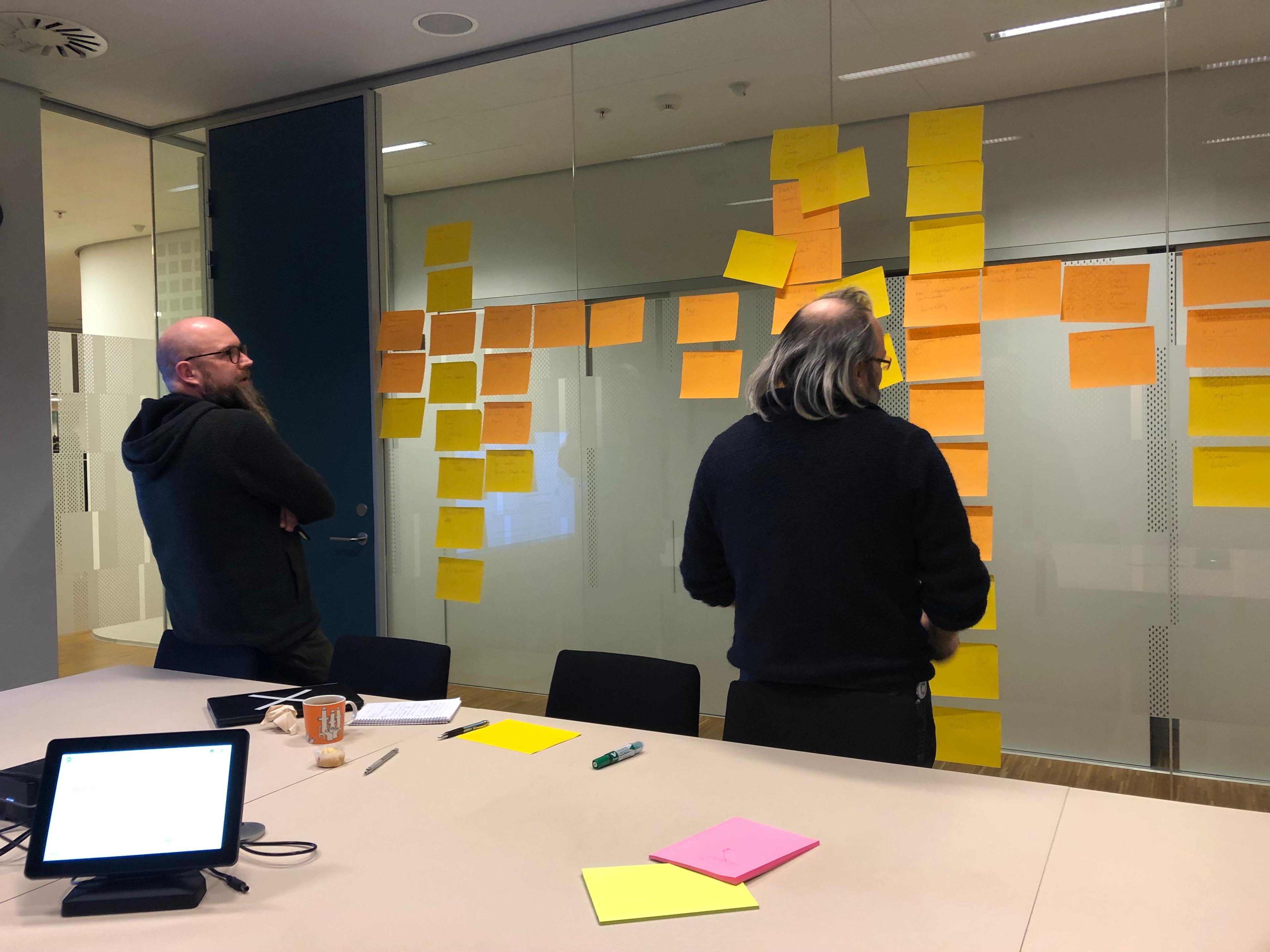 Two people look at a glass wall with many large sticky notes.