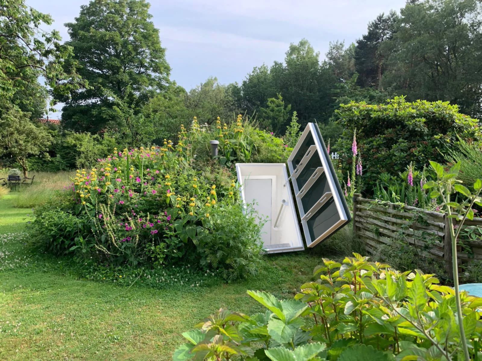 Geöffnete Zugangsluke eines Schutzraums zwischen Gartenstauden