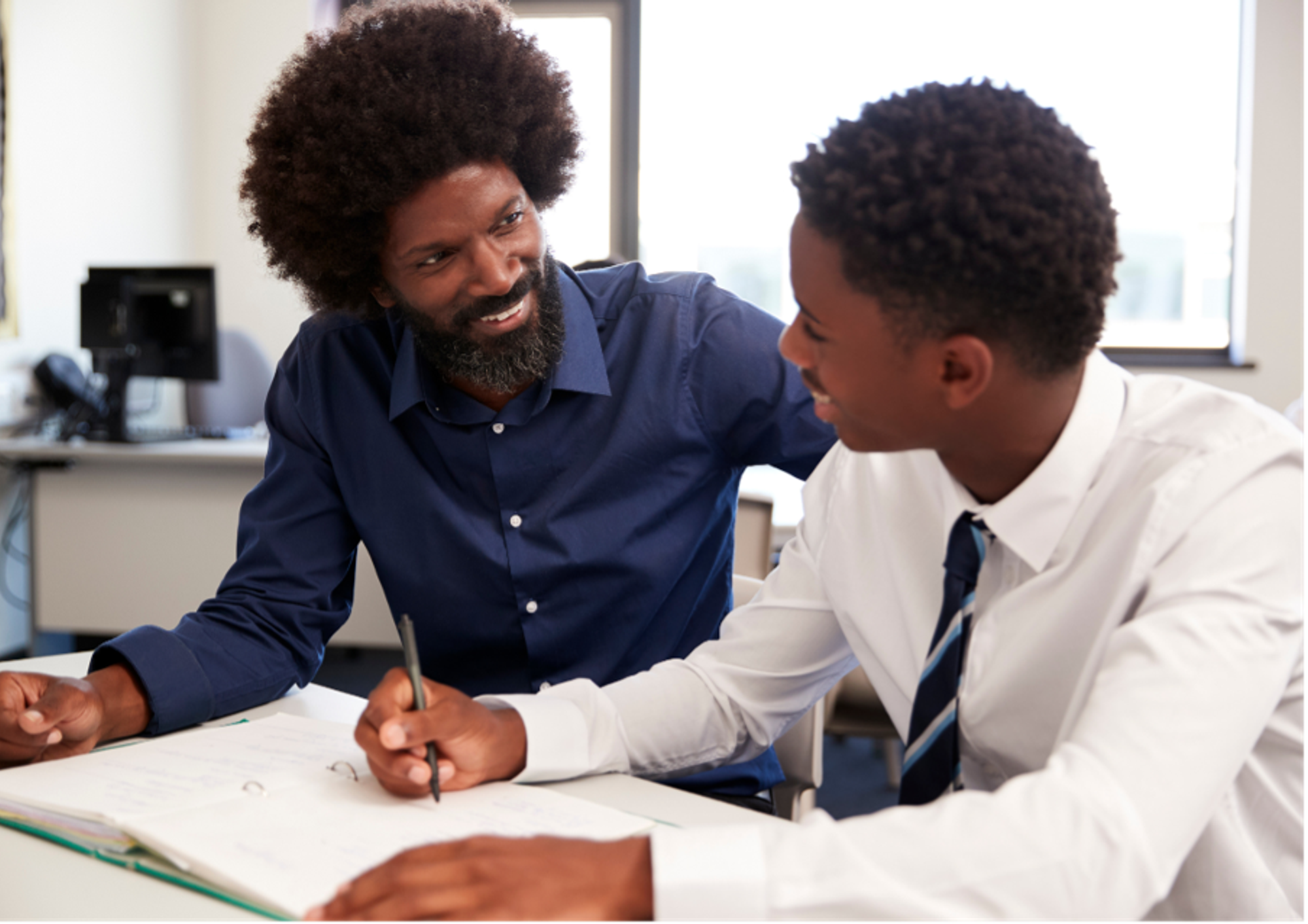 A teacher sitting with a teenage student who is writing.