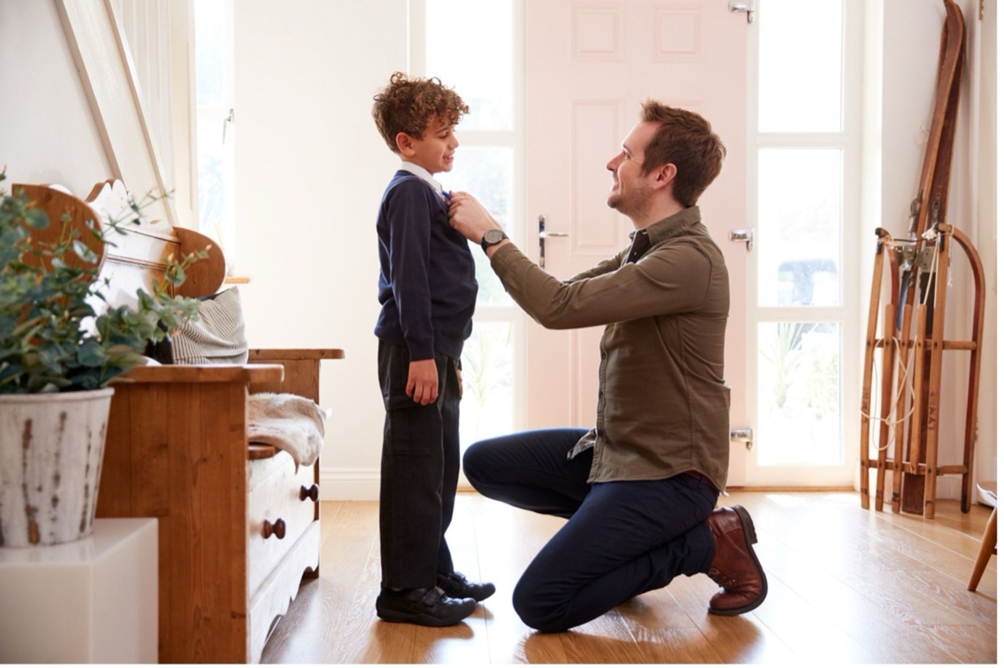 A man fixing a young boy's tie in a house hallway.