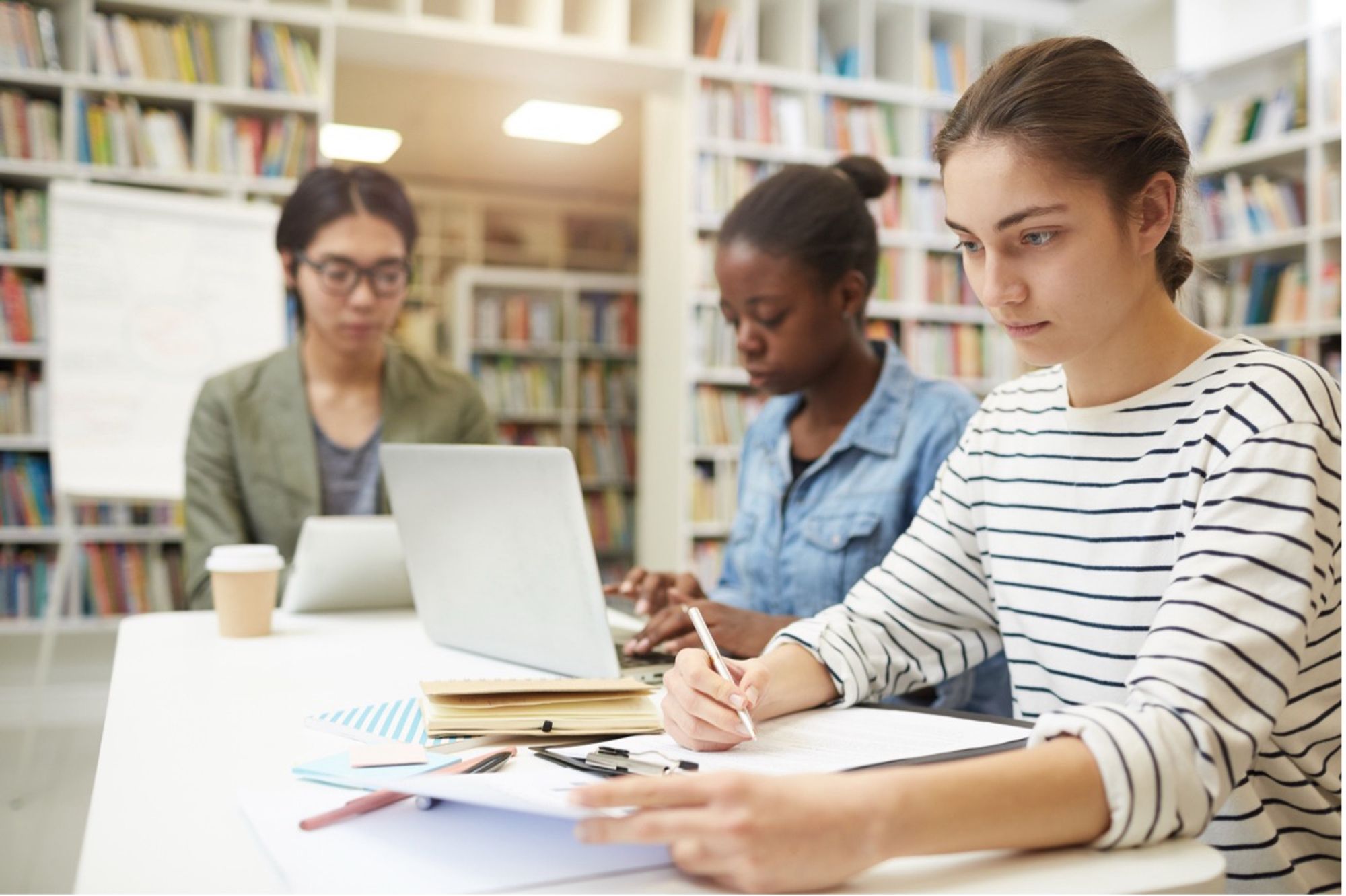 Three college students sitting at a table in a library working.