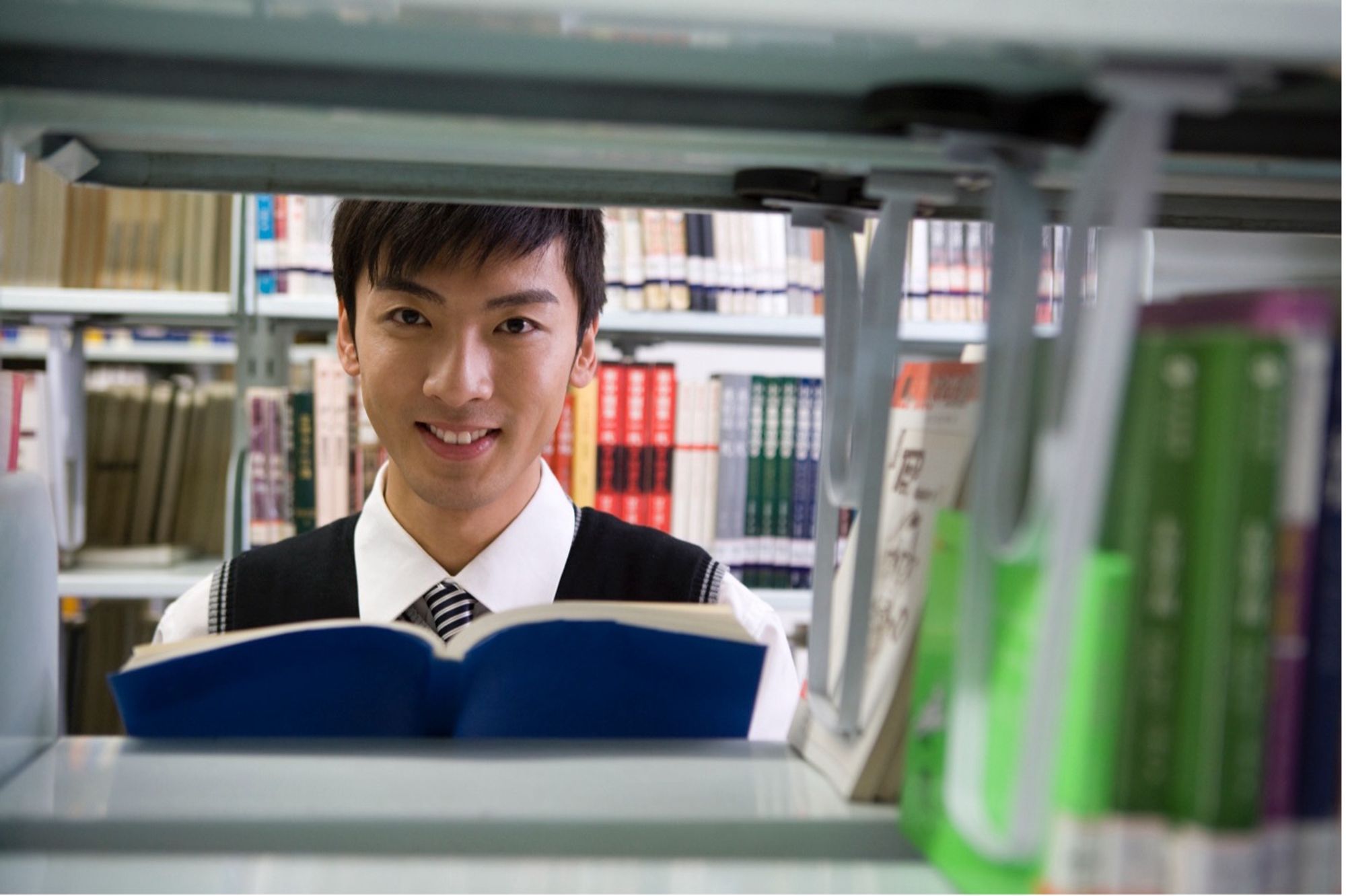 A teenage school boy in uniform reading in a library.