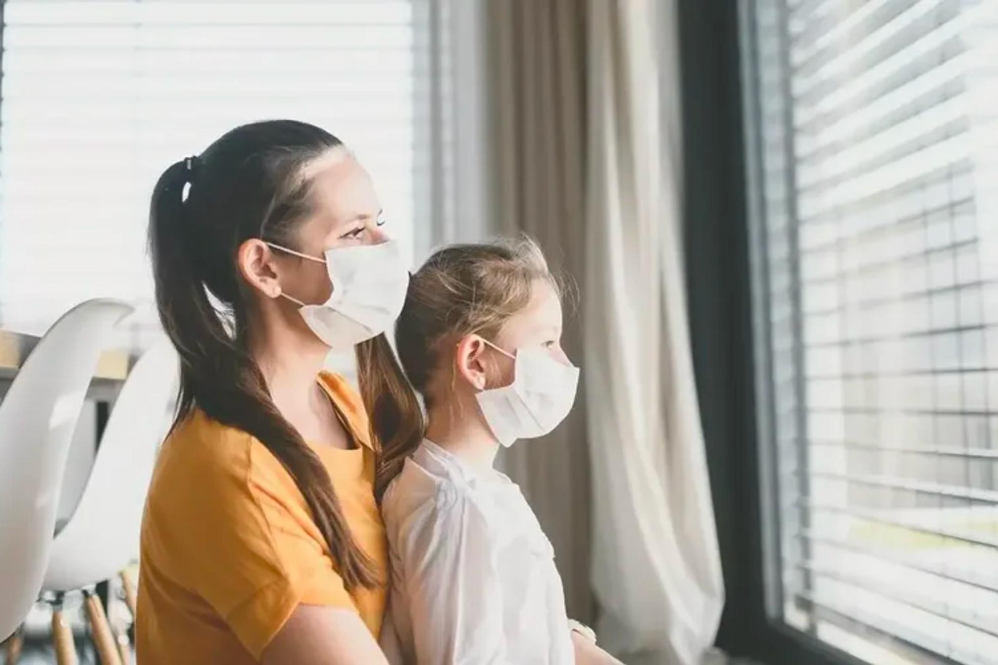 A woman and a child wearing face masks looking out of a window.