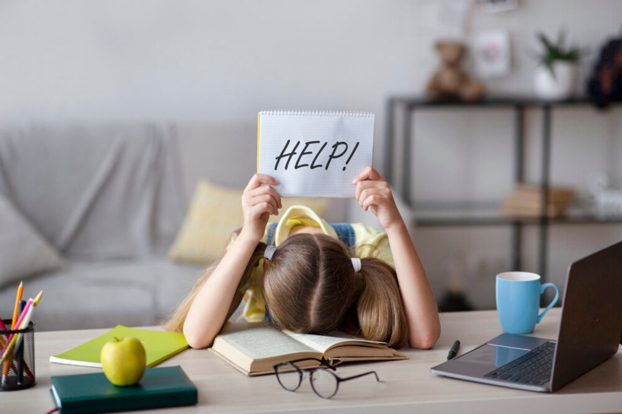 Child with head on desk holding up a sign saying "Help!"