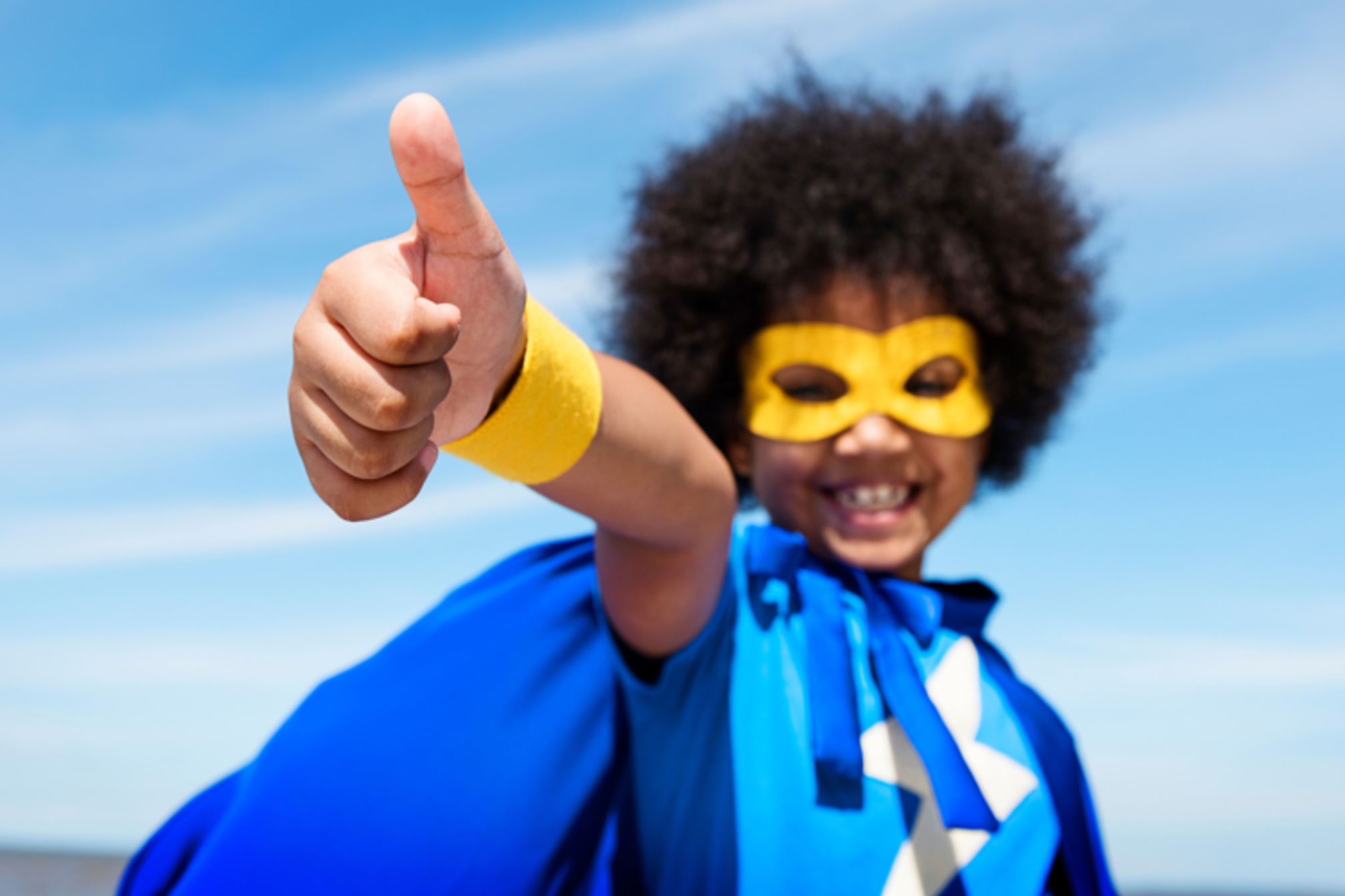A child dressed as a superhero with a cape and mask putting their thumbs up