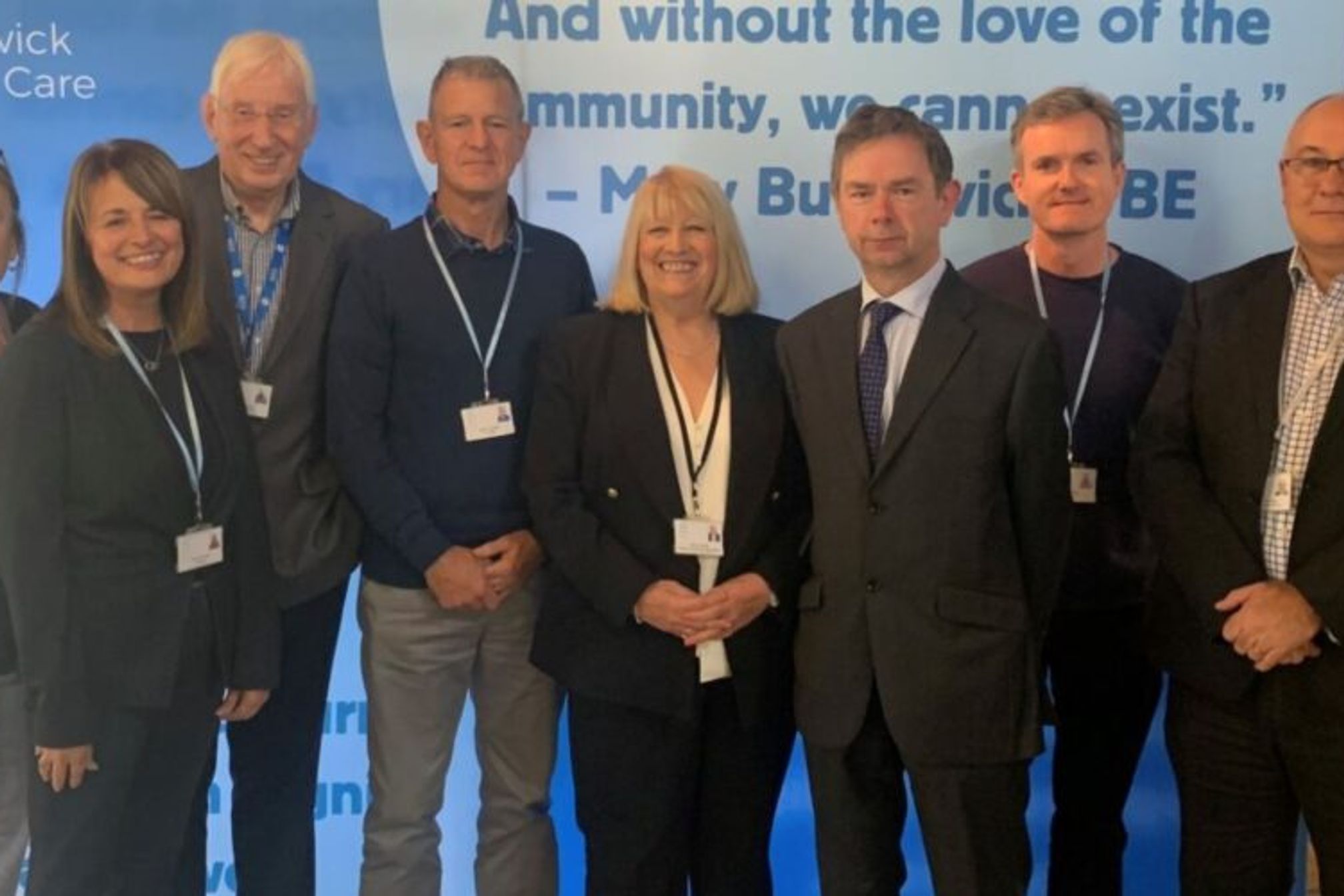 A group of business people wearing lanyards posing for a photograph in front of a Butterwick Hospice Care banner.