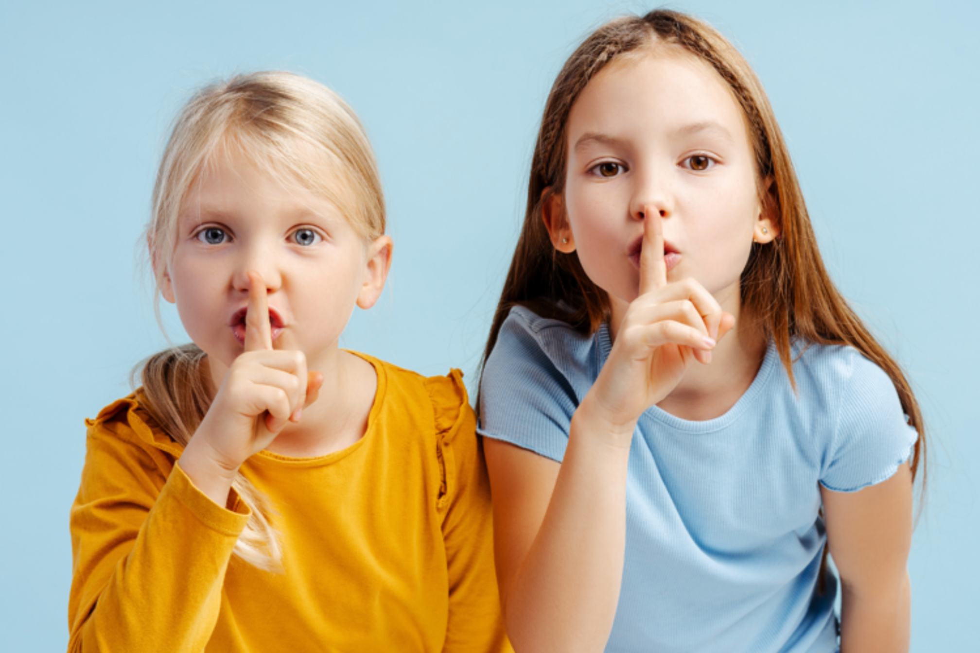 Two young girls looking at the camera holding their fingers to their mouths to say "shhhhh"