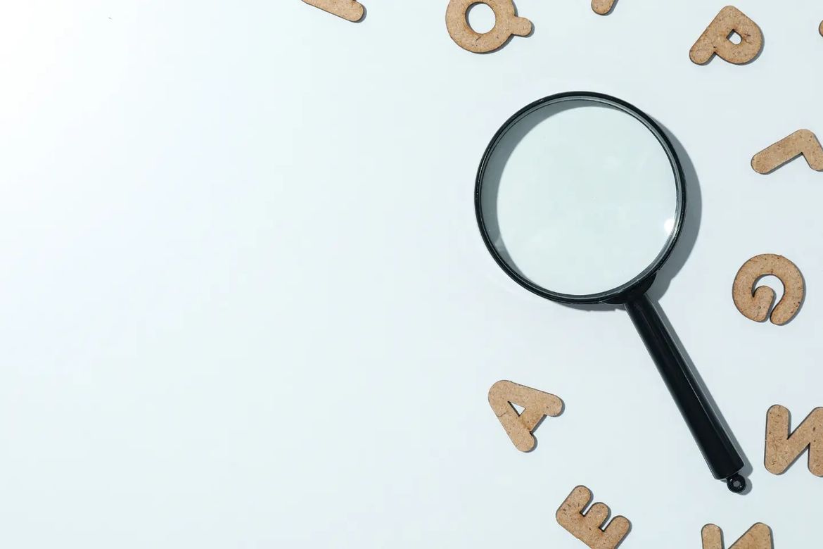A magnifying glass and some wooden letters on a white background.