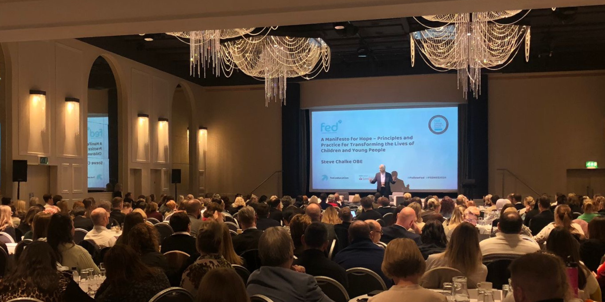 A speaker at a conference in a room full of people.