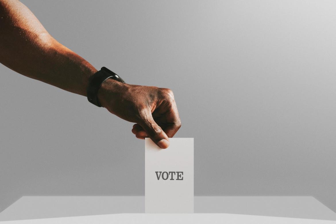 A slip of paper with the word "Vote" being put into a slot in a box.
