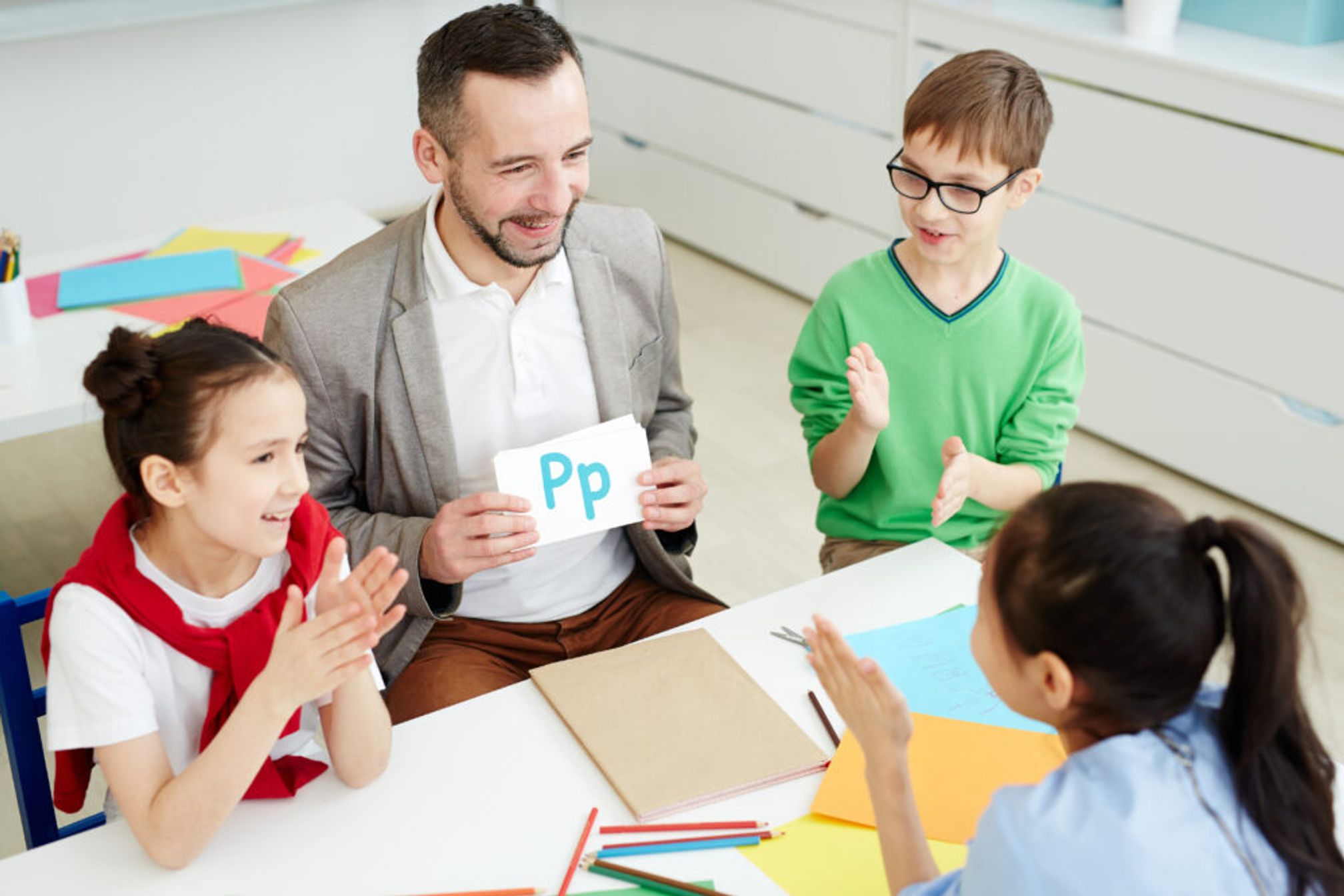 Teacher holding letter cards, sitting with young school children.