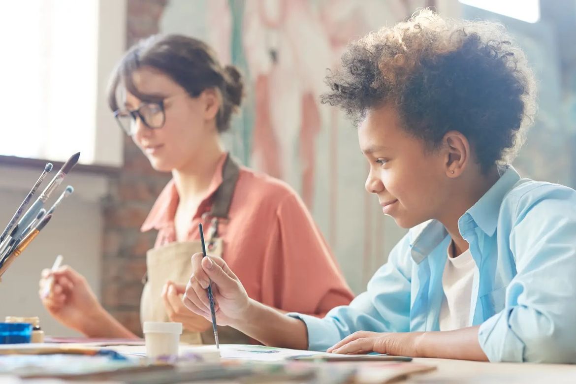 A boy and a girl are sitting at a table painting