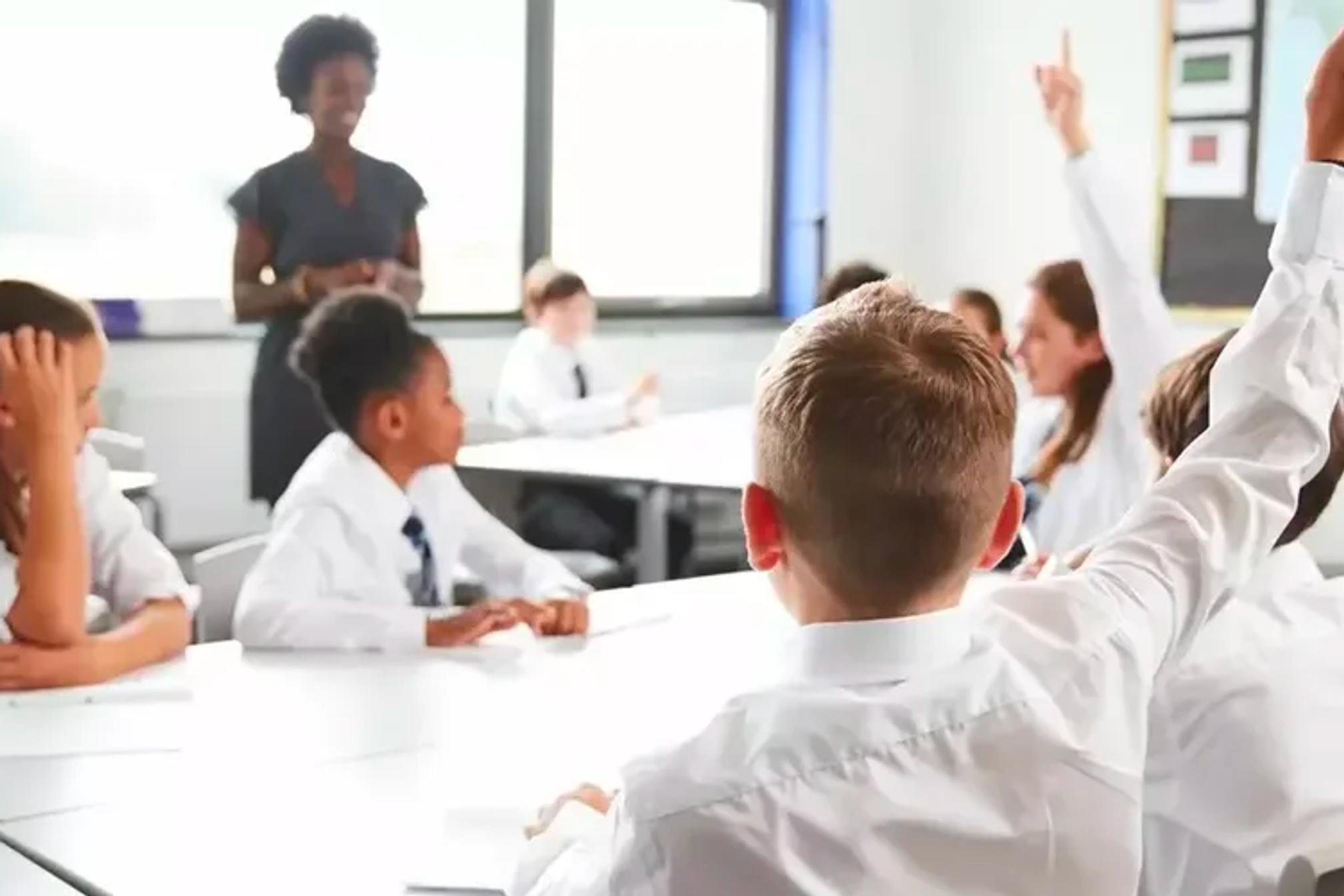 Secondary school students with their hands up in classroom