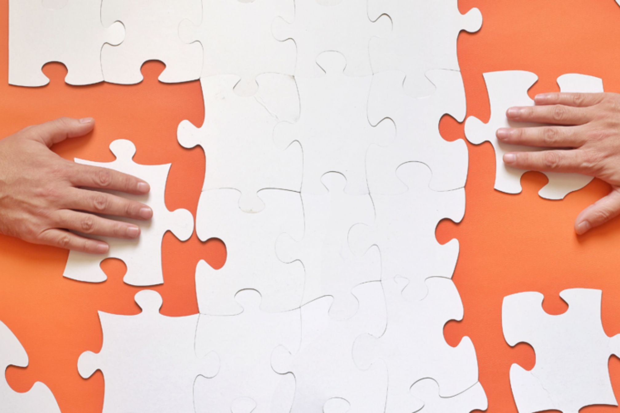 A jigsaw with two hands putting pieces in place.