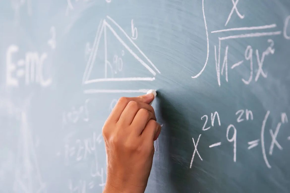 A hand writing mathematical figures on a chalkboard.