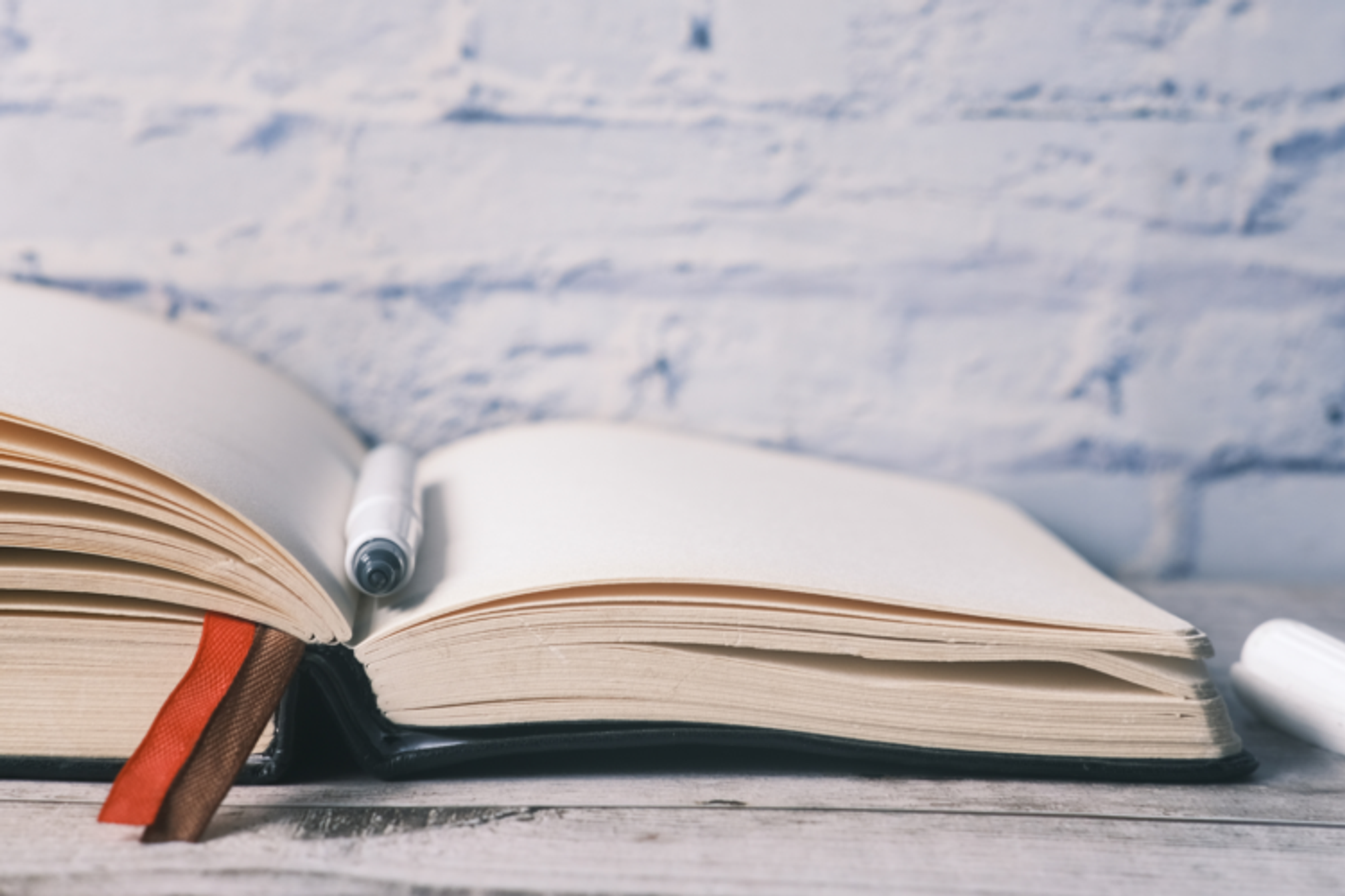 An open hardback notebook with a pen resting in the fold.