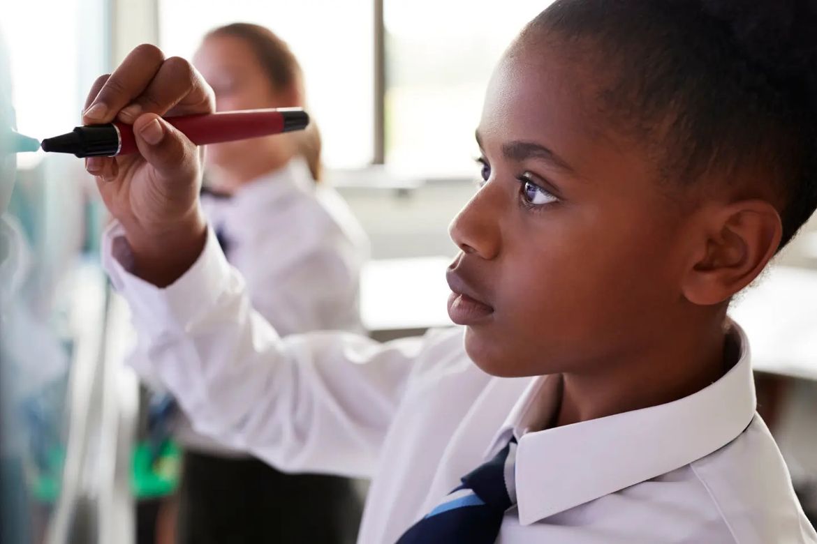 A young secondary school girl is writing on a whiteboard.