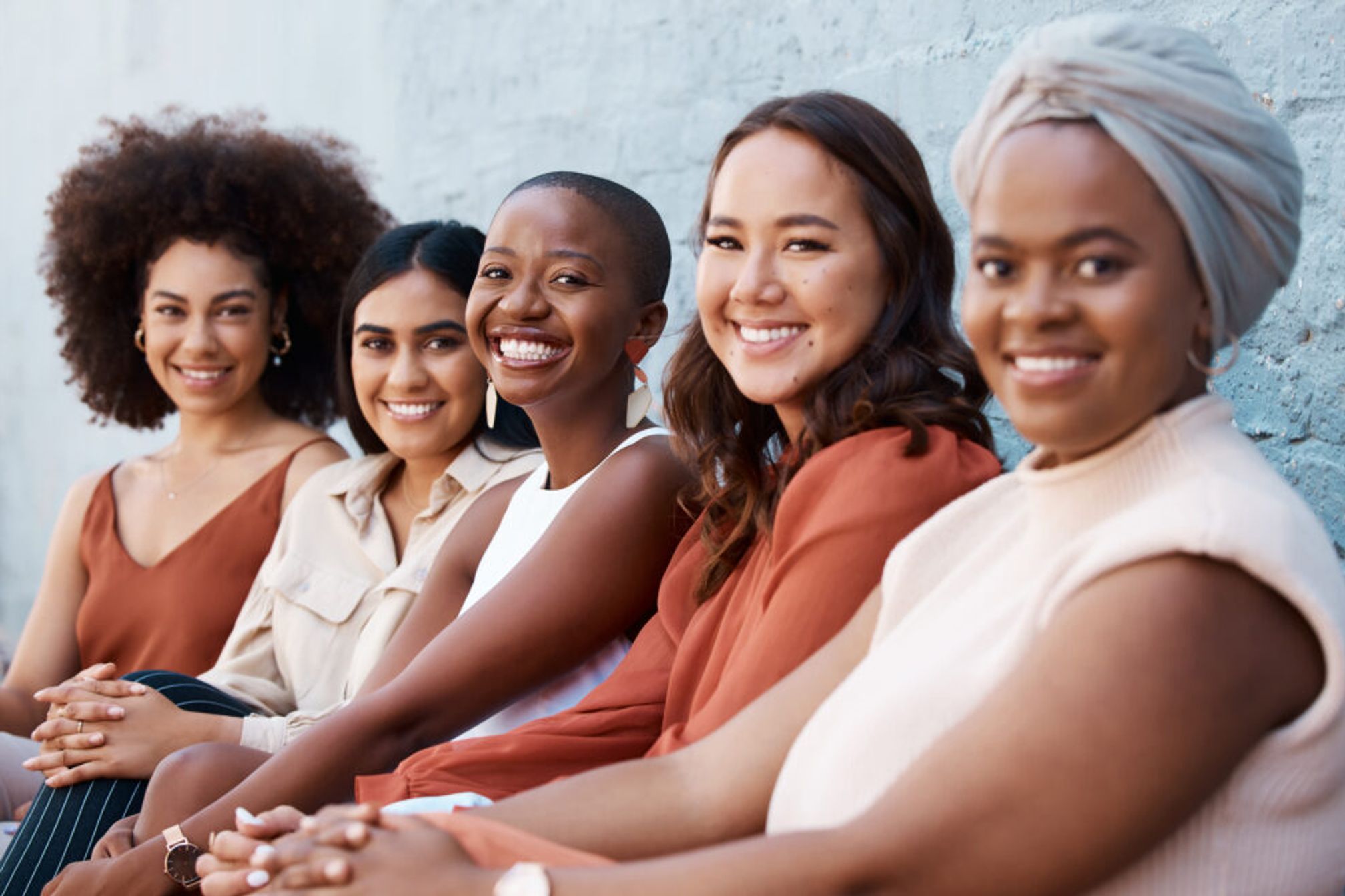 Multicultural women sitting in a row smiling and looking at the camera.