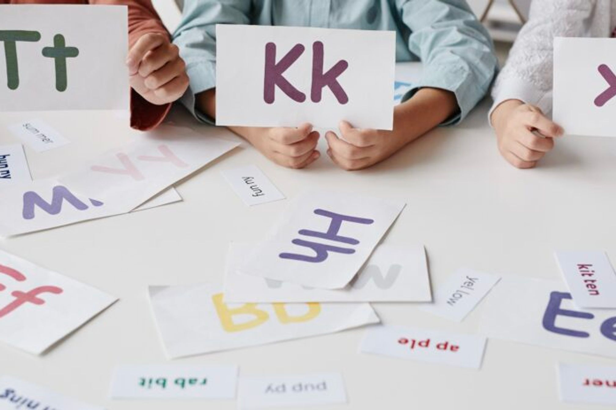 Children sitting around a table holding up coloured card with letters of the alphabet