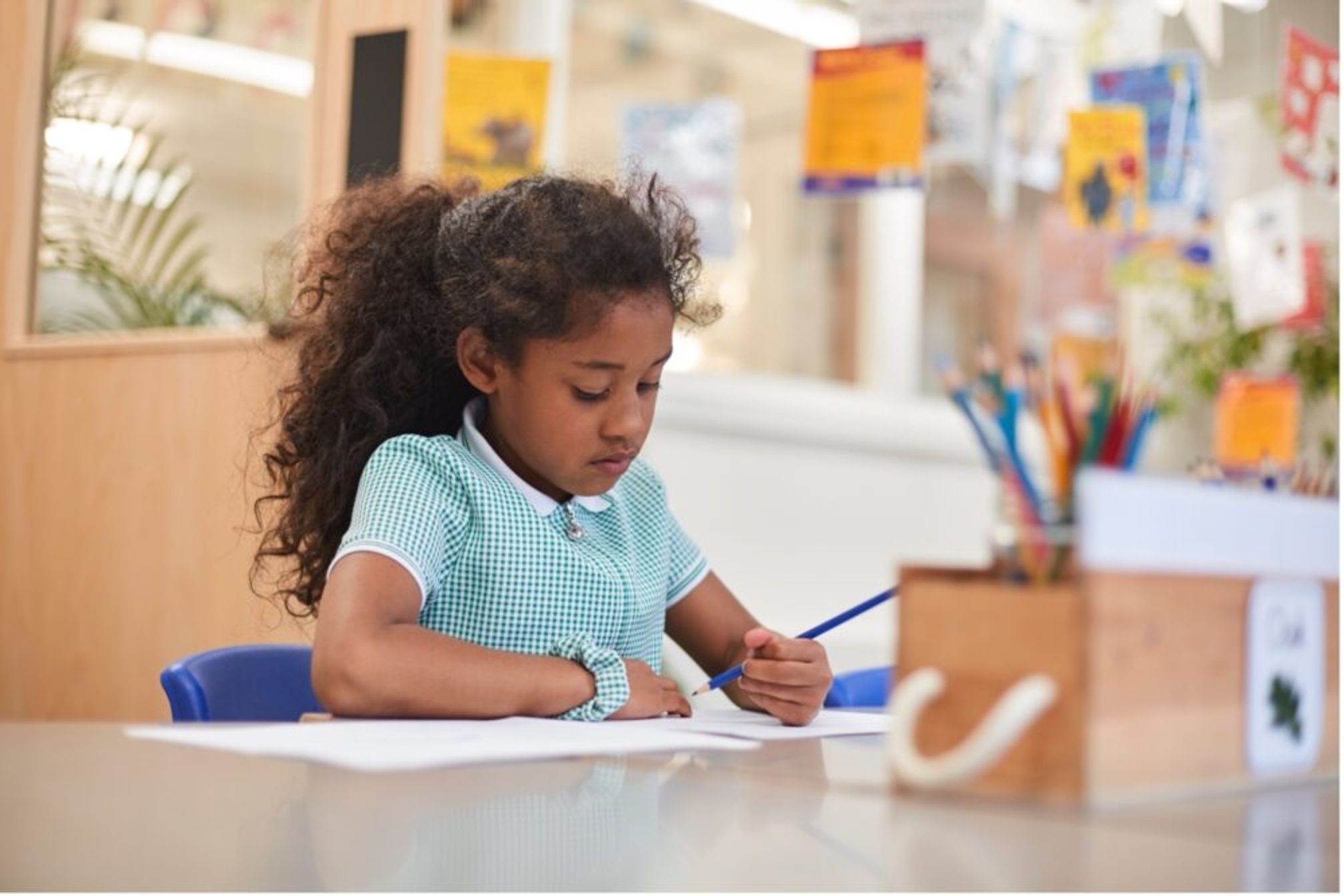 A primary school girl sitting at a table holding a pencil.