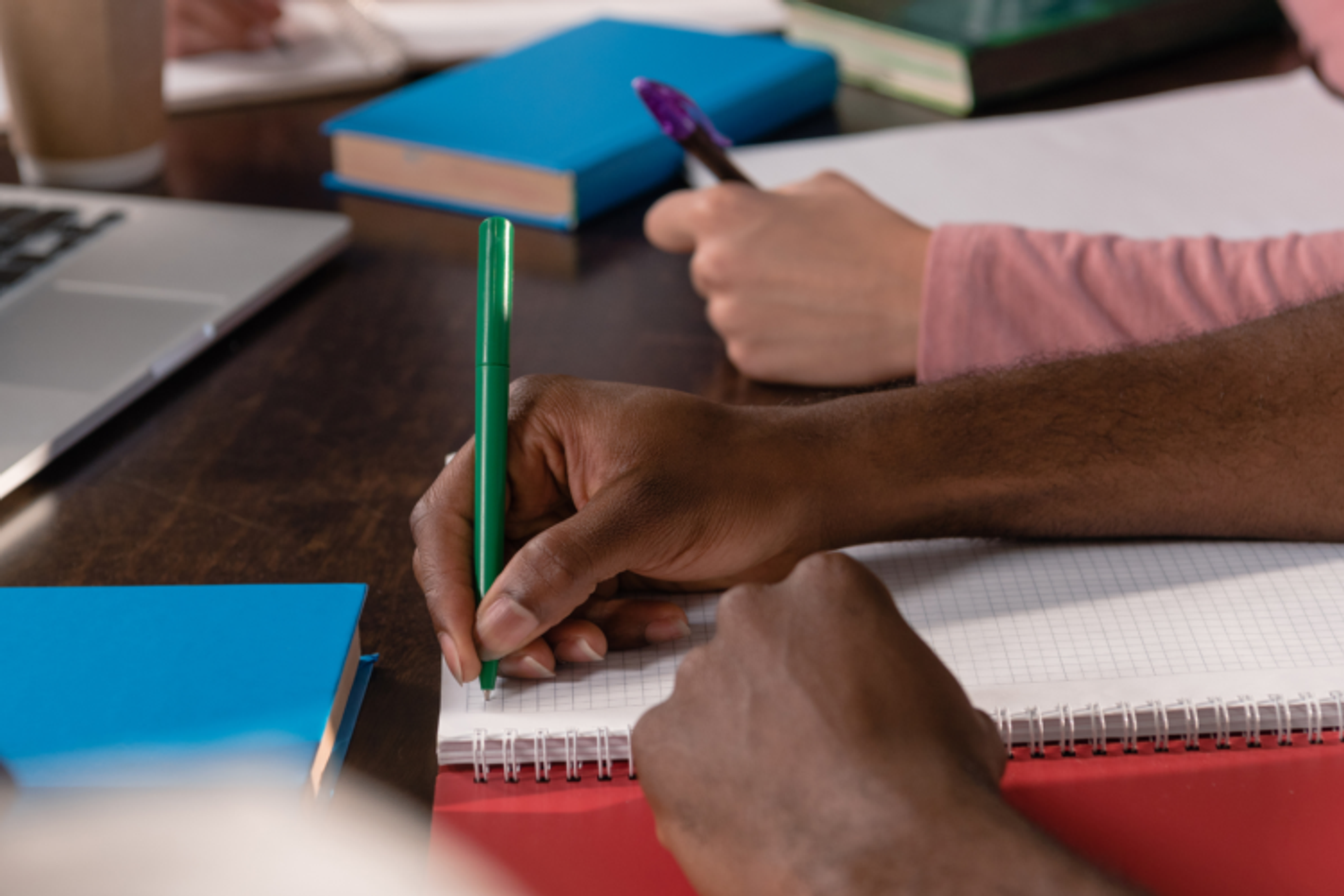 People writing in notebooks on a desk.