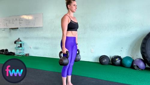 Kindal at the top the of the double kettlebell deadlift with her shoulders pulled back and her butt squeezed and legs locked out.