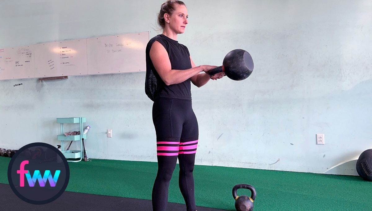 Kindal at the top of the kettlebell swing. Her arms are packed and the kettlebell is at chest height. She if fully locked out in her legs and balanced.