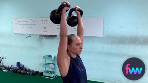 Kindal holding two kettlebells overhead.