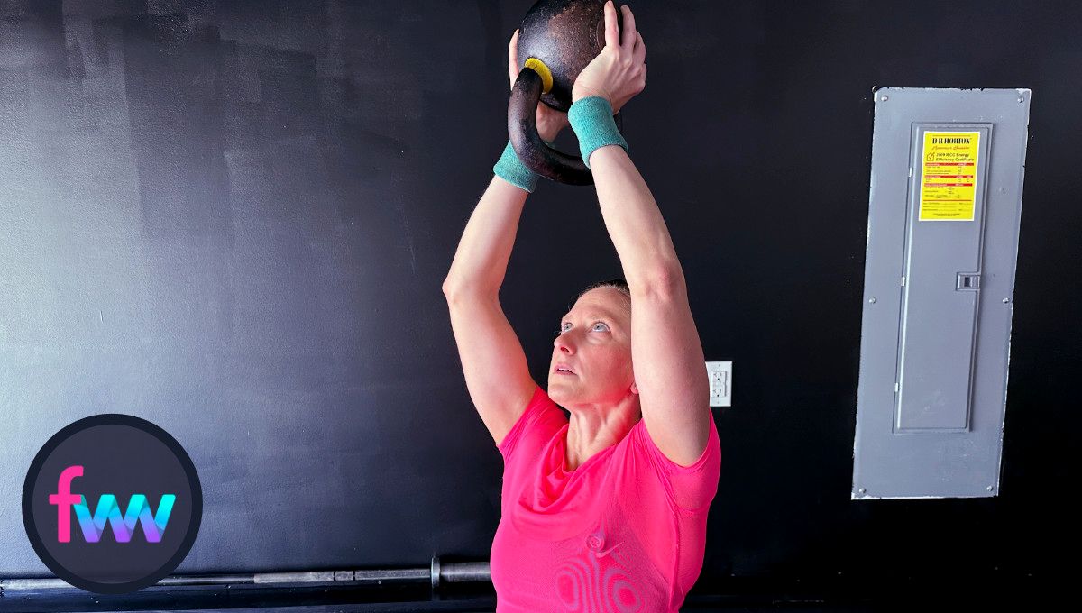 Kindal presses the kettlebell over her head but does not fully lock out her arms. She keeps her core tight so her low back does not arch too much.