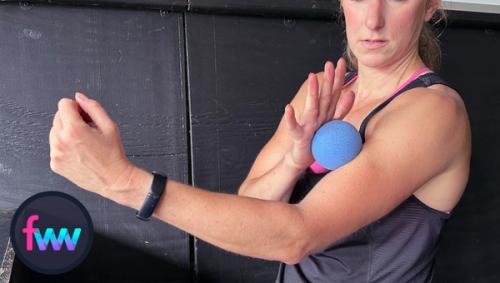 Kindal is using the trigger ball to smash into her bicep muscle with her other hand. She is working to loosen up her bicep which can cause the tricep to get really tight.