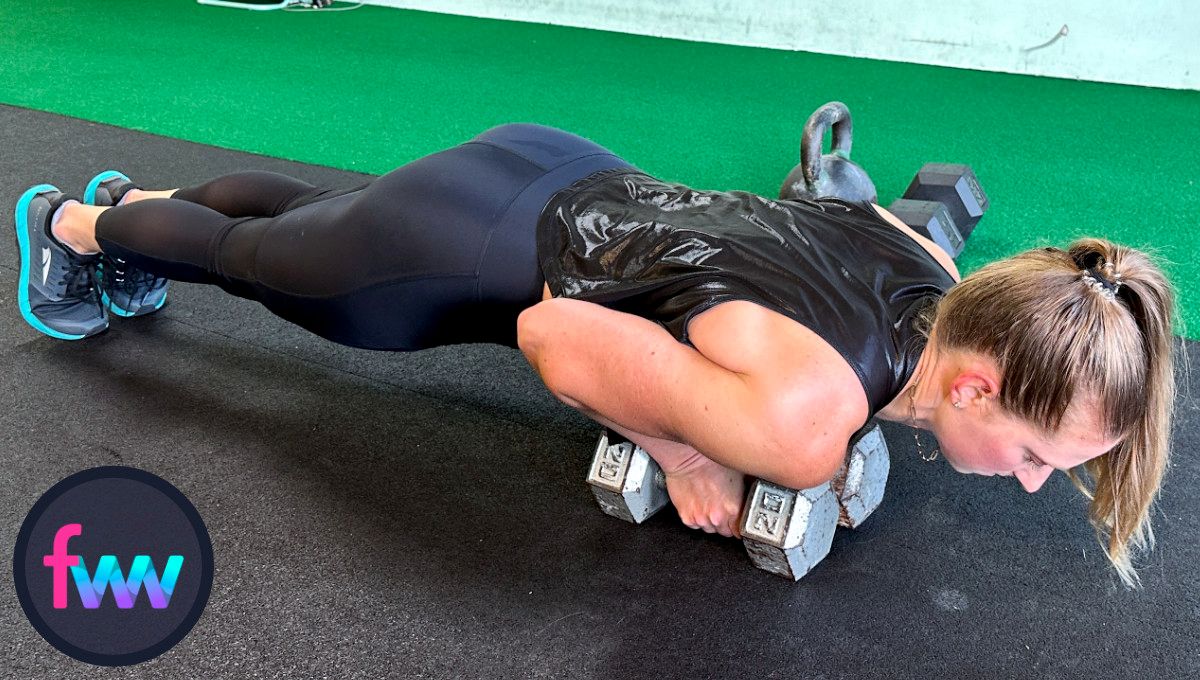 Kindal at the bottom of double dumbbell close grip pushups. Her chest is directly over the dumbbells and her body remains very straight with her legs and core engaged.