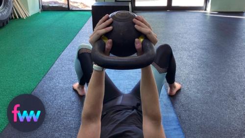 Kindal showing how to hold a single kettlebell during the floor press.