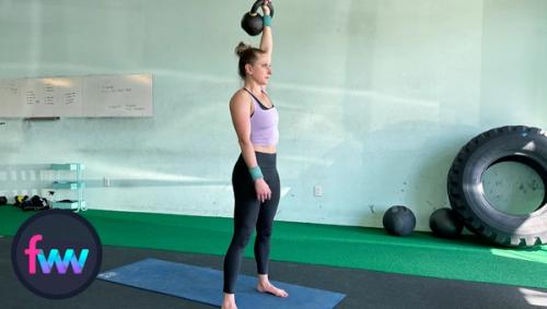 Kindal stands up by pushing into her toes and front foot and comes all the way up while still extending the kettlebell up in the sky.