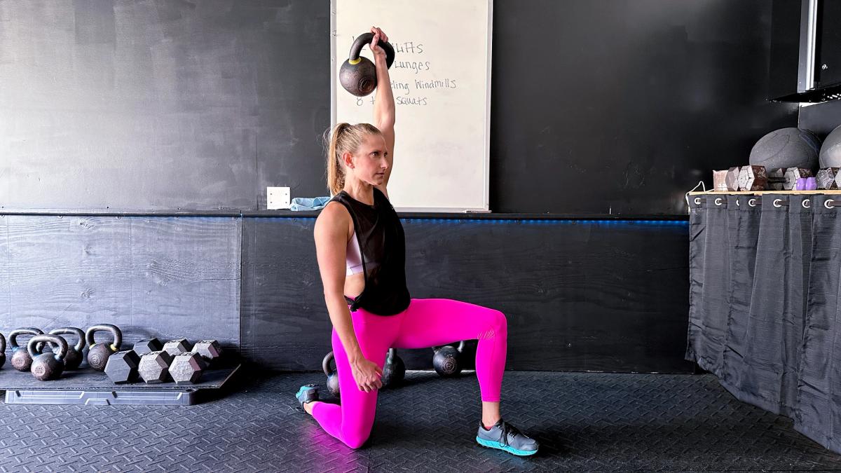 Kindal in the kneeling position and pressing the kettlebell over her head. Her body is engaged ready for the windmill.
