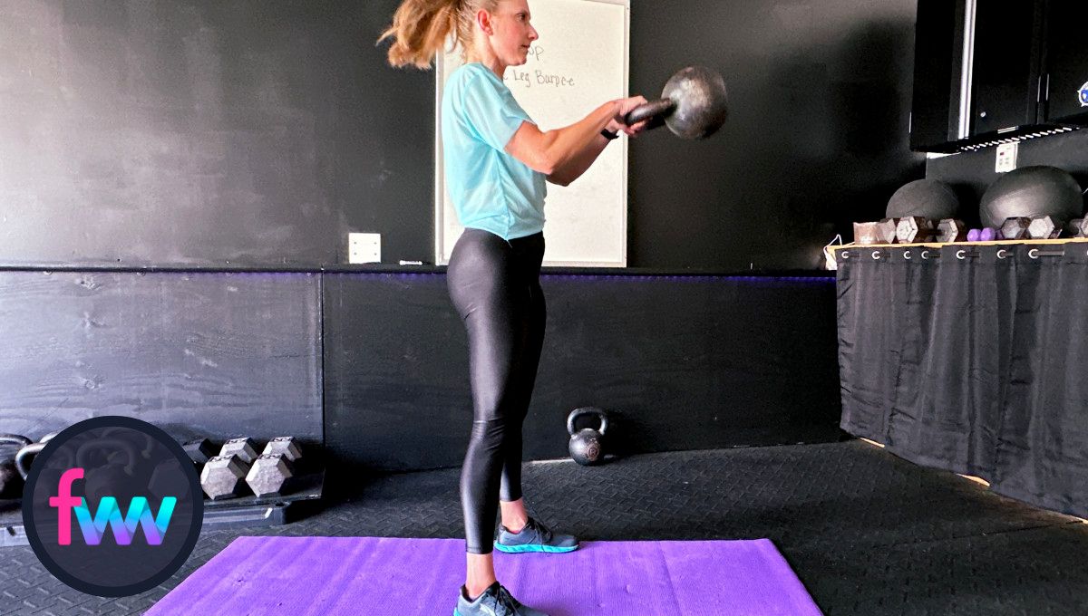 Kindal at the top of the kettlebell swing fully locked out and kettlebell at chest height and her body in near perfect balance.